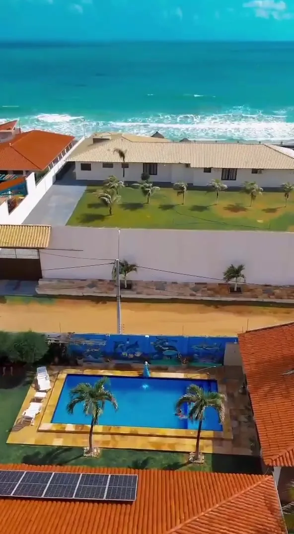 Vista aérea mostrando o telhado e a piscina da Casa Bem-te-vi, a fileira de casas da frente e o mar logo atrás