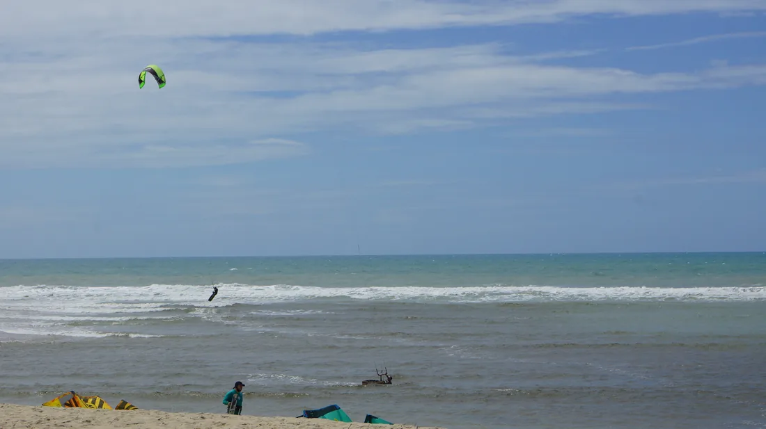 Pipa de kitesurf no alto e praticante cortando a água, na praia de Aquiraz, no Ceará