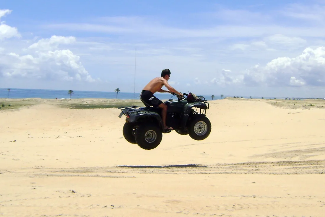 Quadriciclo saltando uma duna de areia, com o mar e os coqueiros ao fundo