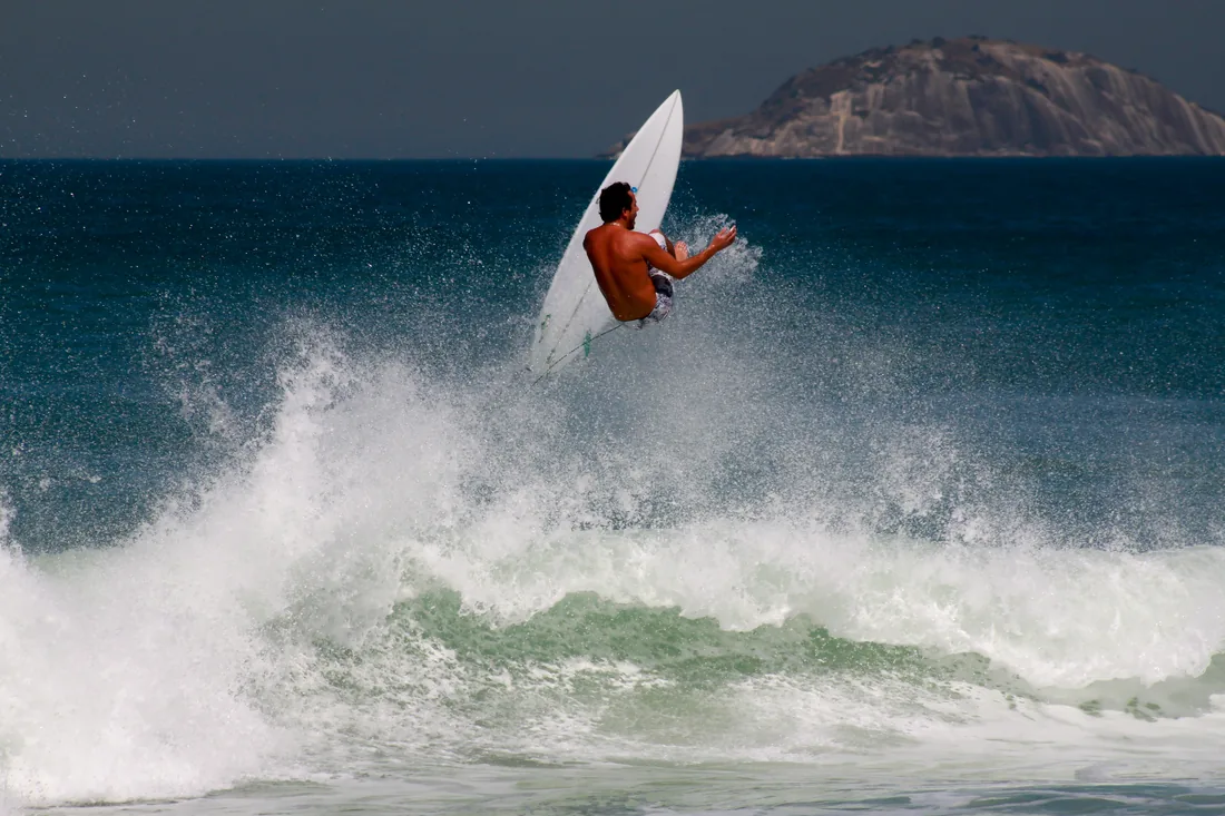 Surfista fazendo uma manobra na crista da onda, com o mar azul ao fundo