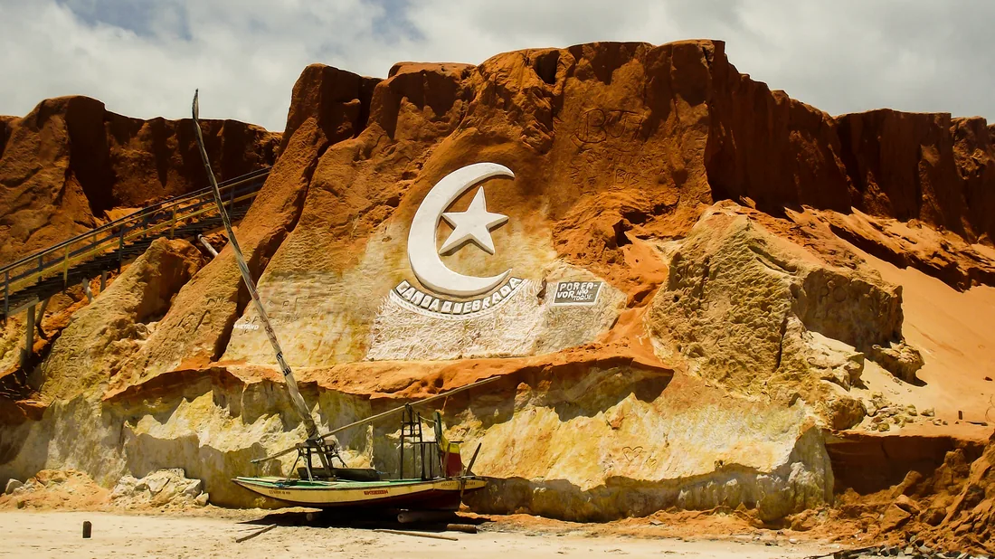 A falésia vermelha de Canoa Quebrada com o símbolo da lua e da estrela, e uma jangada na areia