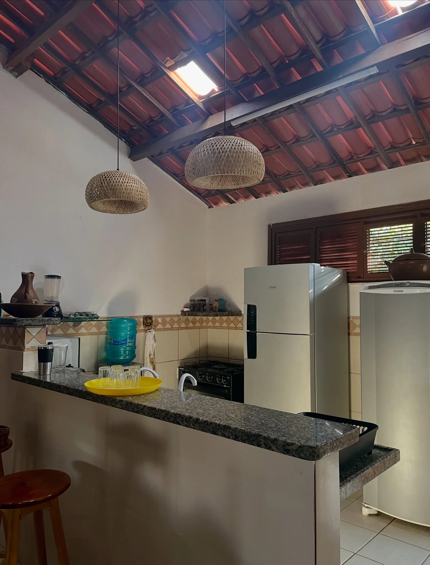 Cozinha da casa com bancada de granito, geladeira e luminárias de fibra
