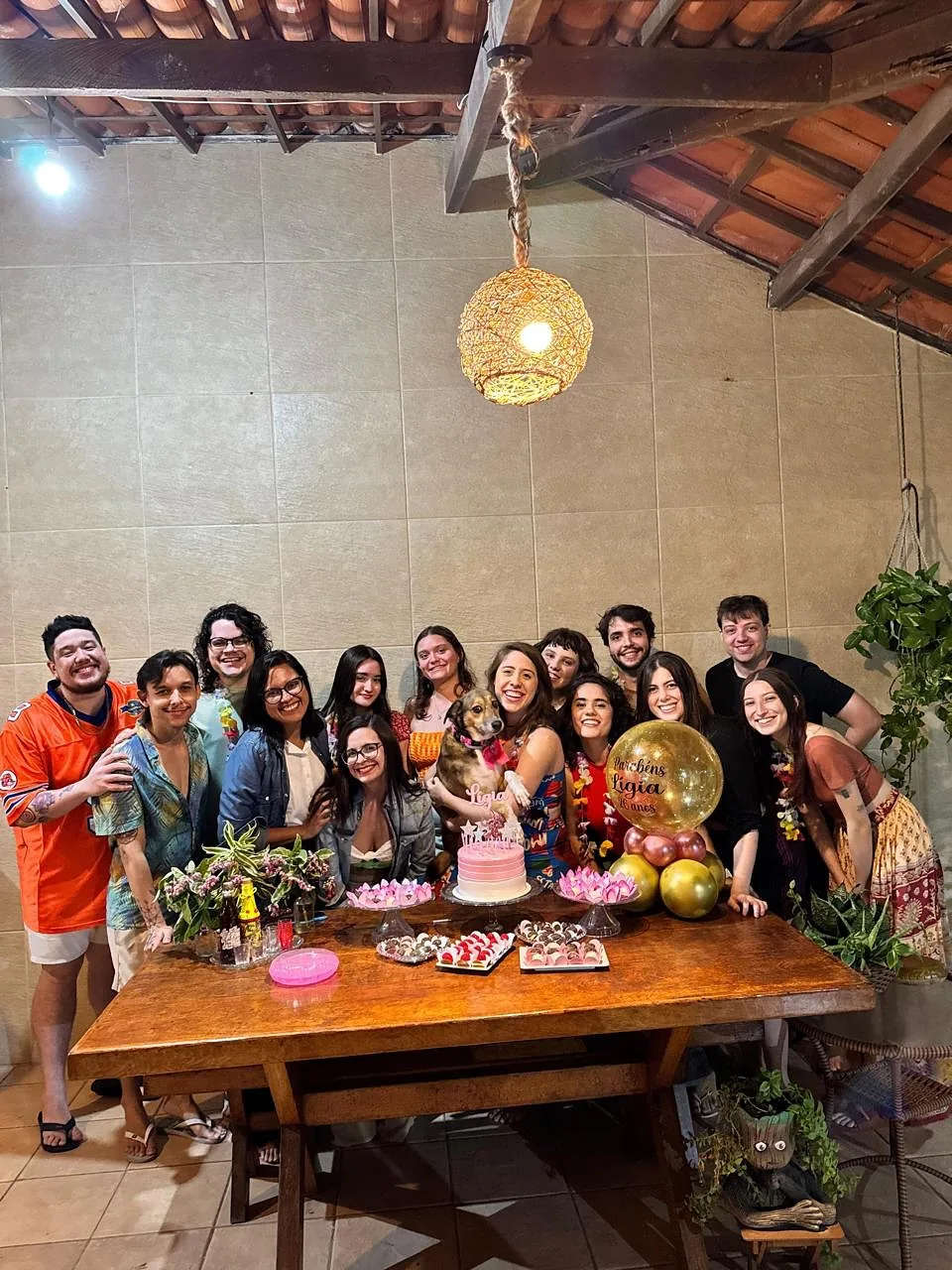 Turma reunida em volta da mesa comprida do deck, sob as luminárias de fibra