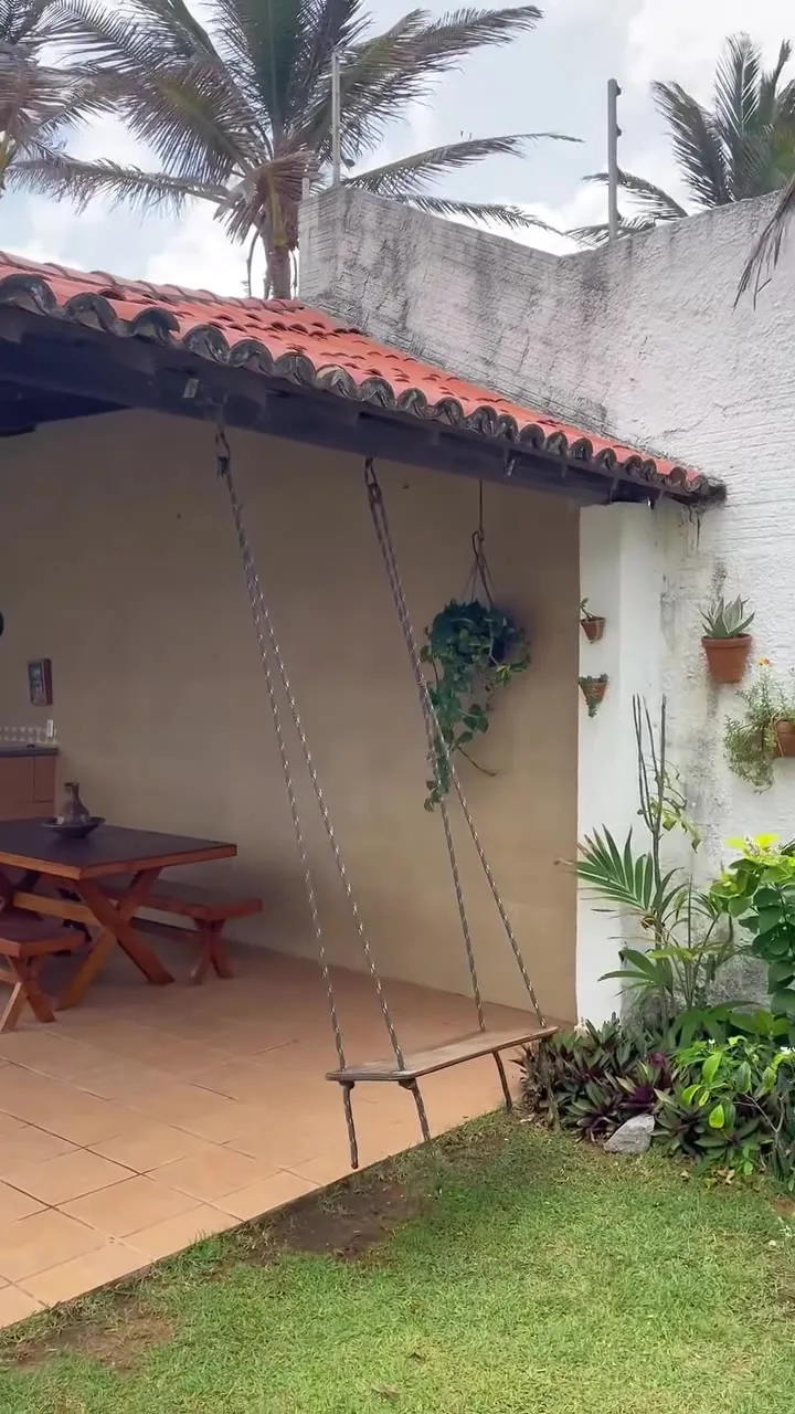 Balanço de madeira no jardim, com o telhado de telha ao fundo