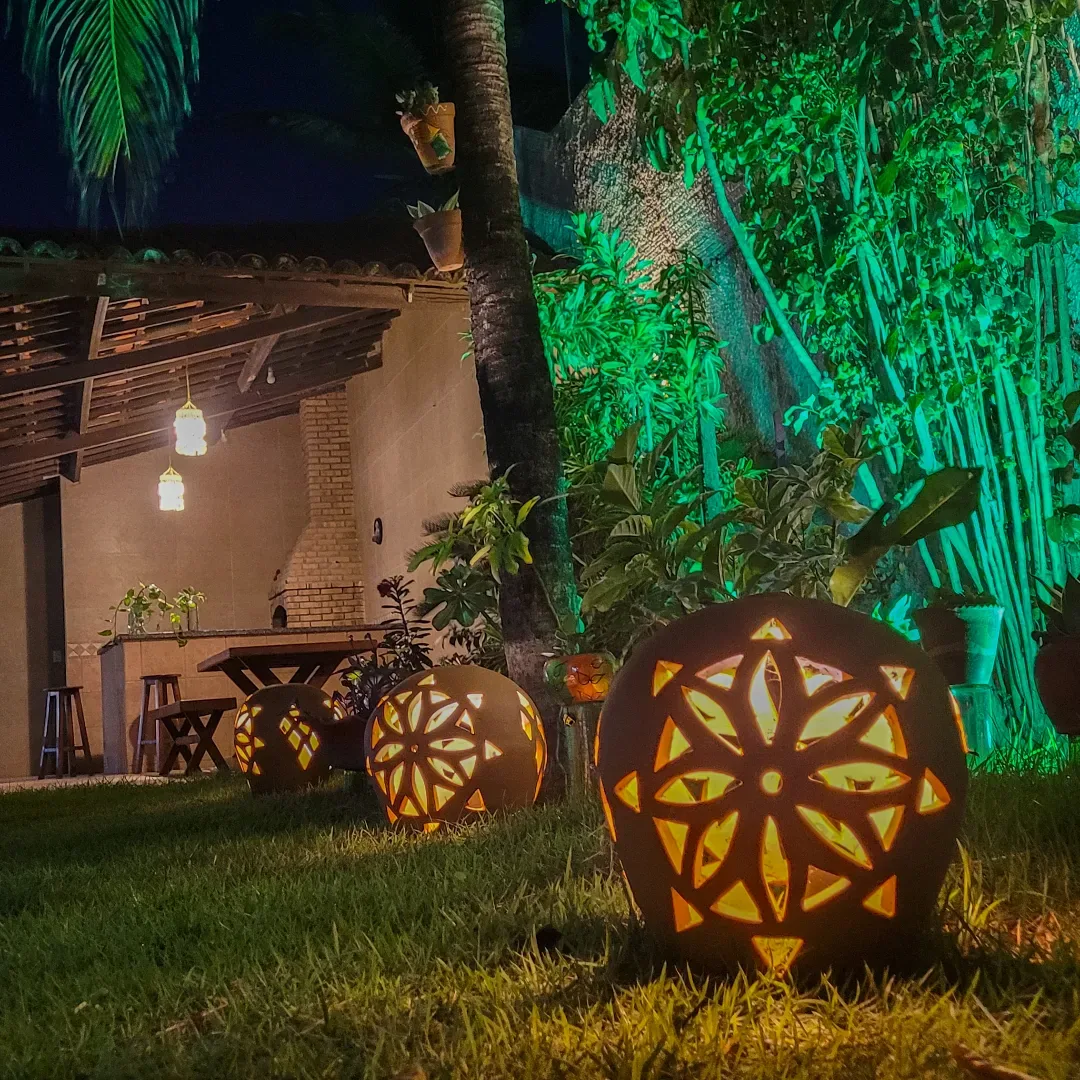 Canto do jardim à noite, com luminária de barro vazado e bambu iluminado de verde