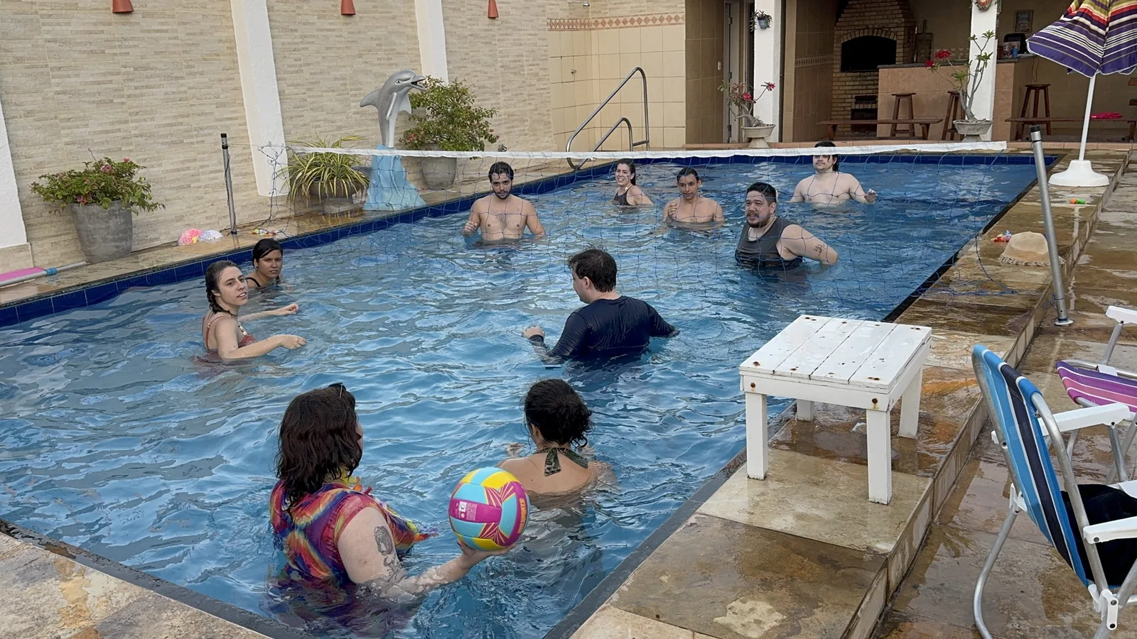 Hóspedes na piscina jogando bola, com o deck e a churrasqueira ao fundo