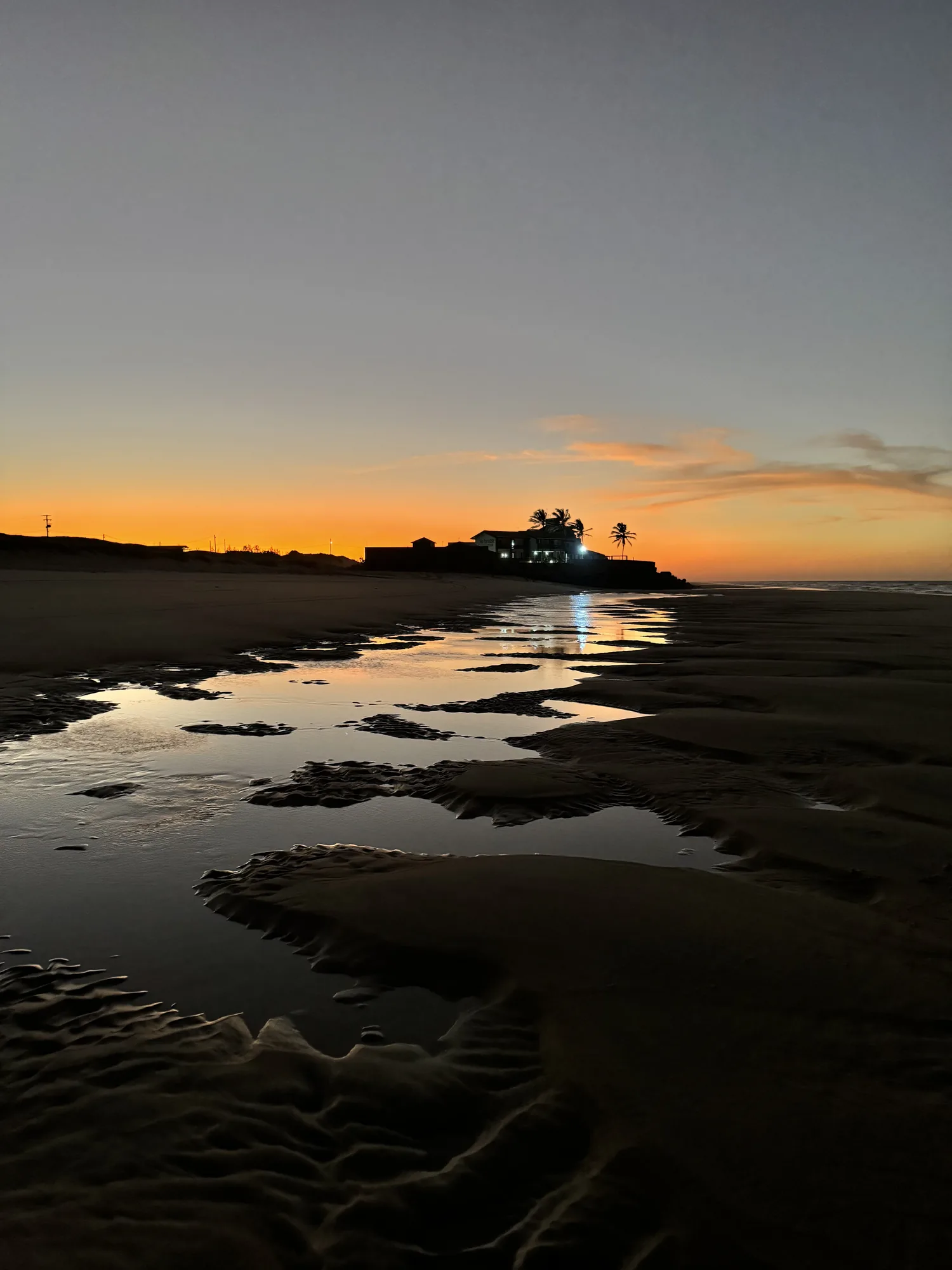 Fim de tarde na Praia da Caponga, com poças de maré refletindo o céu laranja