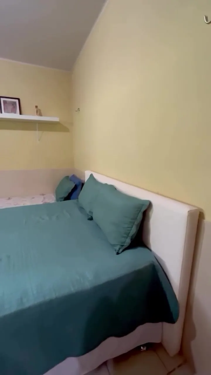 Quarto com cama de casal, colcha verde e prateleira na parede